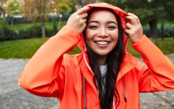 woman wearing a bright orange raincoat pulling the hood up over her head