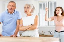 grown up daughter looking animated with her finger in the air as she says something to her parents in the kitchen