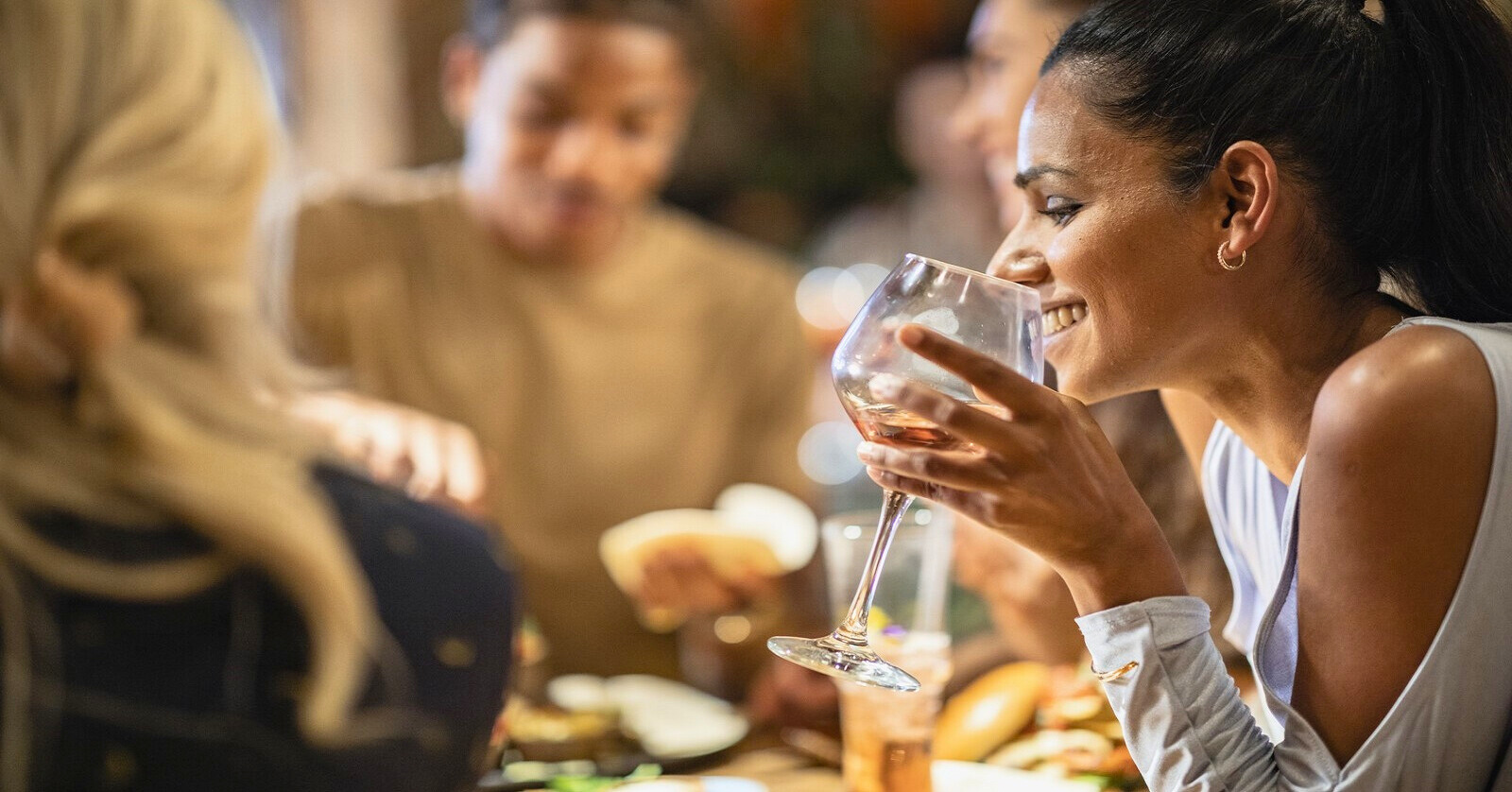 smiling woman sitting around the dinner table with friends holding a glass of wine