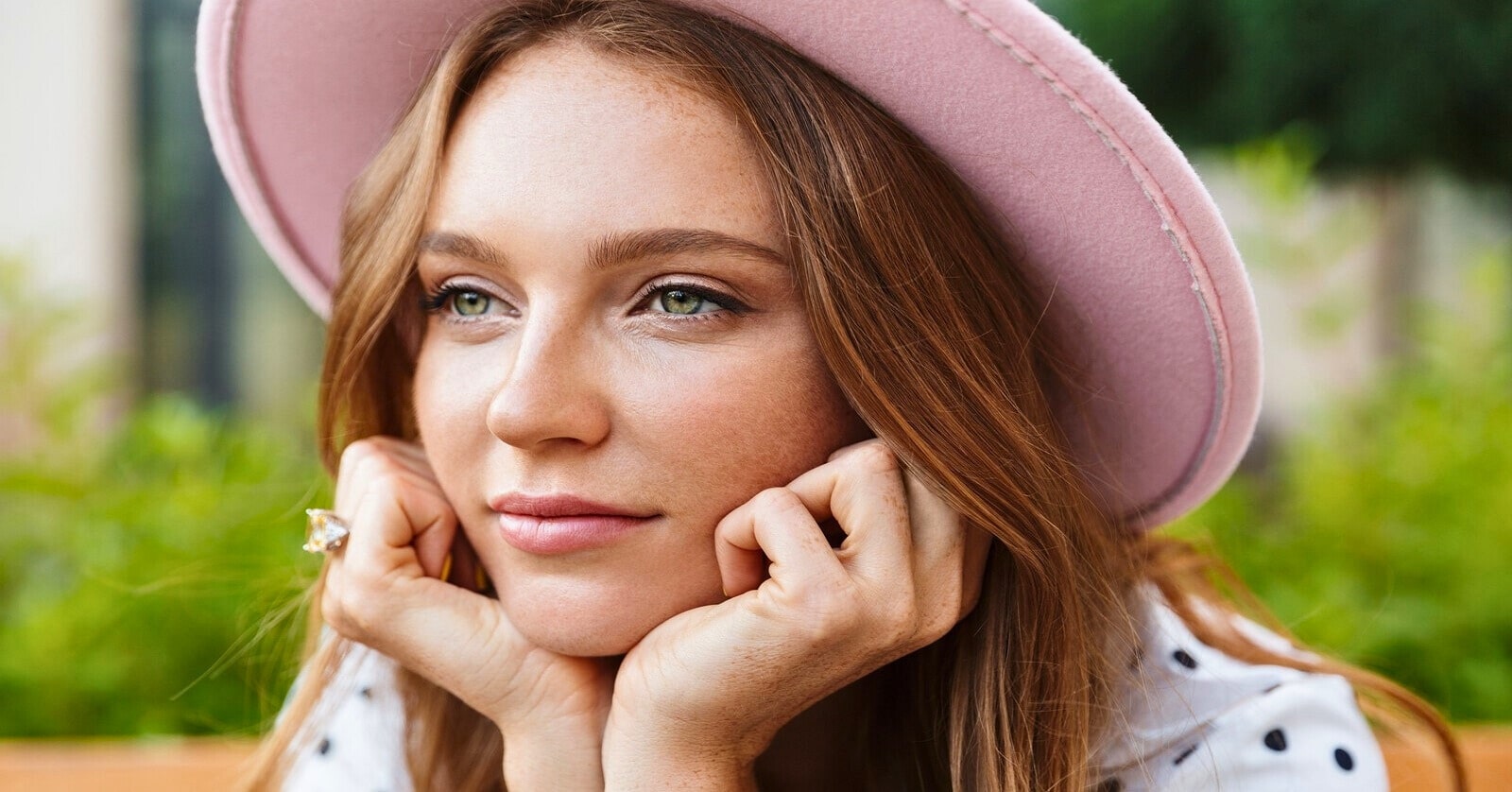 content woman wearing a pink hat resting her head on her hands - she is not looking for love