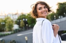 young smiling woman wearing white blouse looking over shoulder as she walks outside