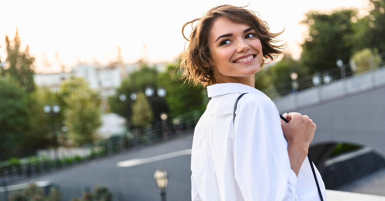 young smiling woman wearing white blouse looking over shoulder as she walks outside