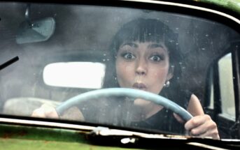 young brunette woman with funny look on her face sitting in a vintage but rusting old car