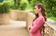 woman wearing pink cardigan standing on garden path with crossed arms looking none too happy