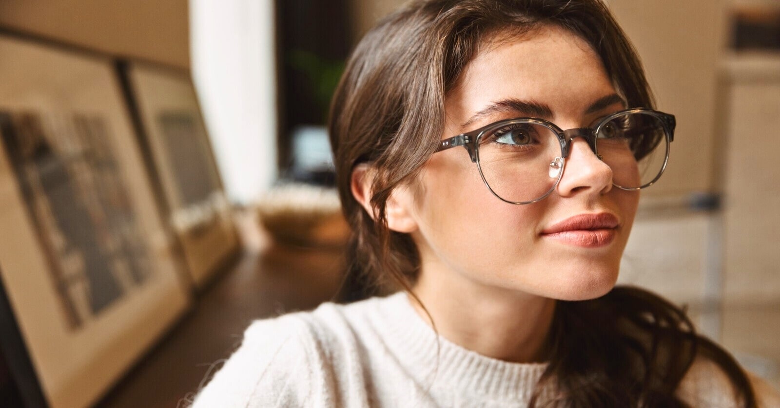 young brunette woman with glasses with some framed artworks in the background