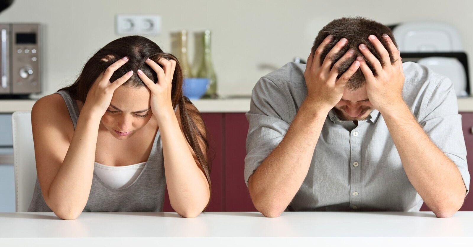 couple sitting a kitchen counter, both with their head in their hands because the relationship is not good
