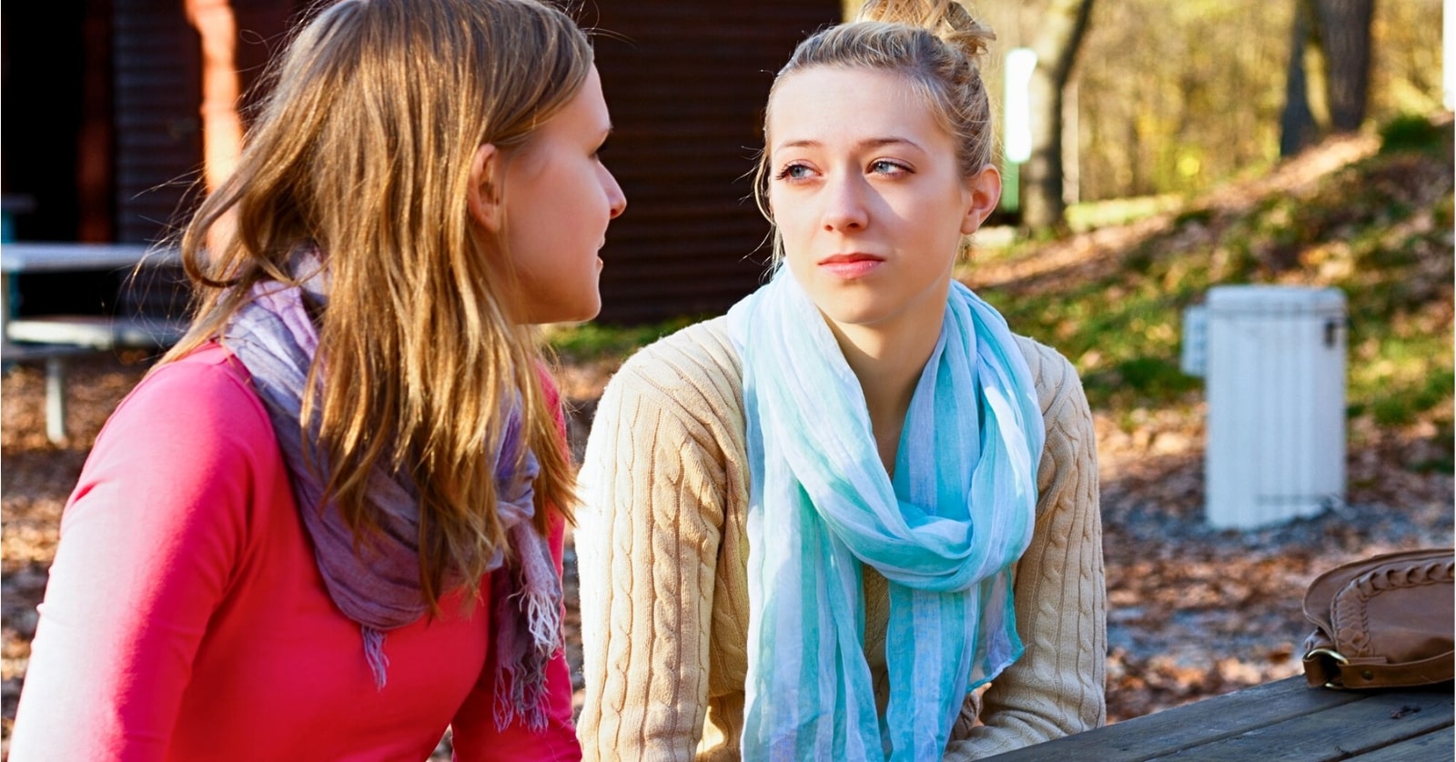 two women in their twenties talking while sitting on a bench outdoors