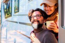 middle-aged man and woman looking happy as they stand by their campervan in a natural setting