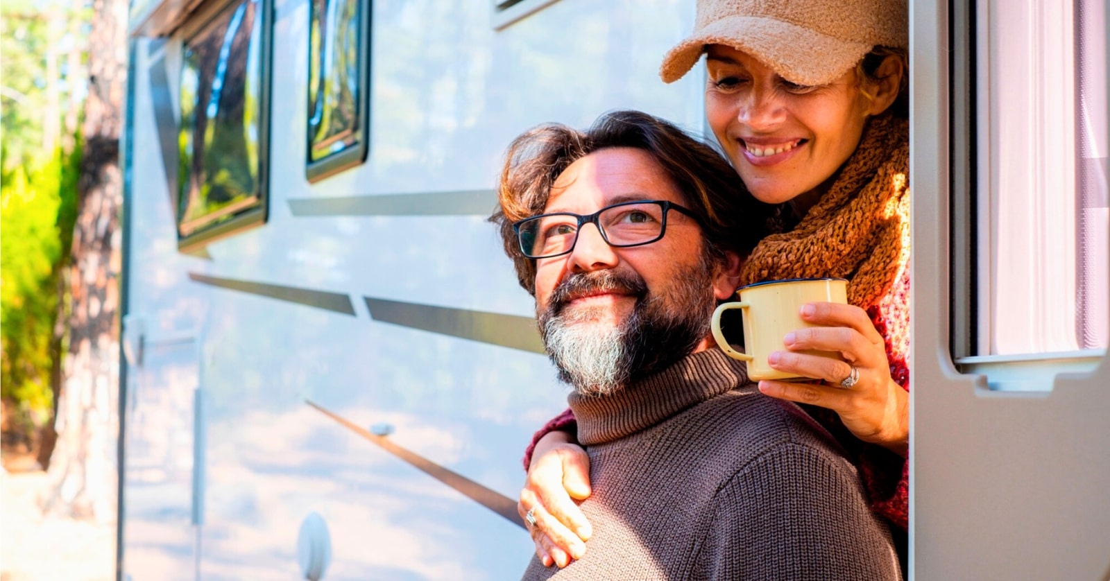 middle-aged man and woman looking happy as they stand by their campervan in a natural setting