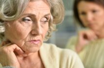 senior mother with look of resentment on her face with her grown daughter in the background