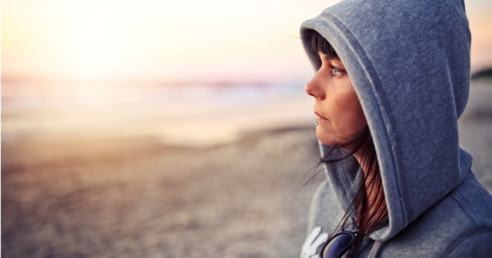 pensive women in a blue hoodie at the beach reflecting on her people-pleasing tendencies
