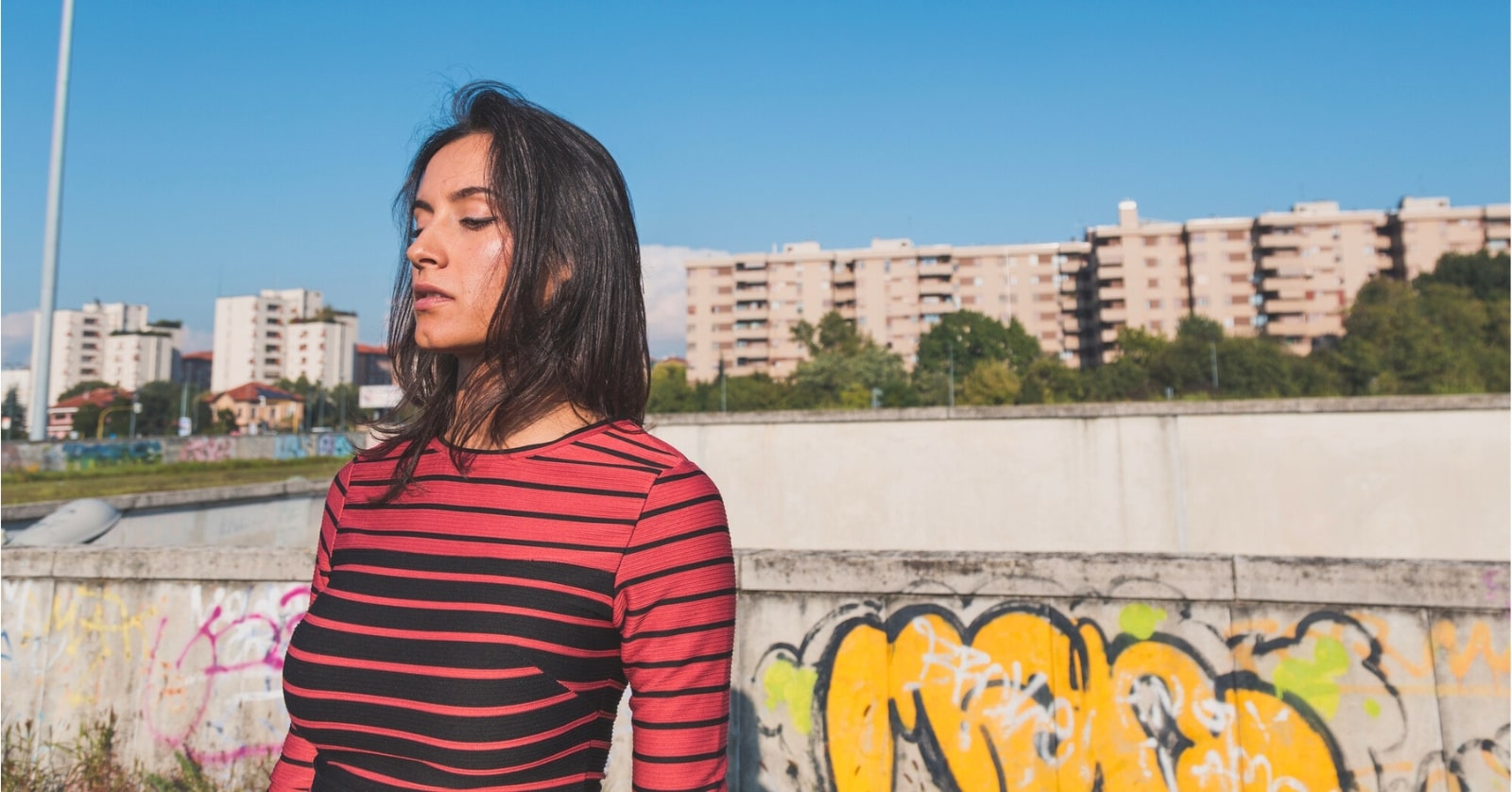 woman wearing red top standing in front of some graffiti with buildings in the distance