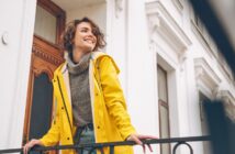 smiling woman wearing bright yellow coat standing outside townhouse