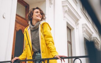 smiling woman wearing bright yellow coat standing outside townhouse