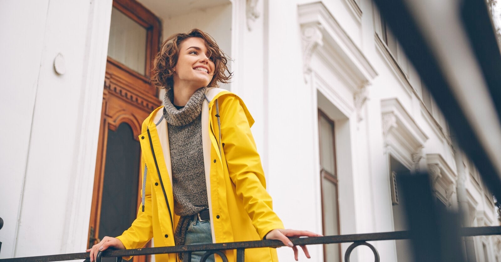 smiling woman wearing bright yellow coat standing outside townhouse