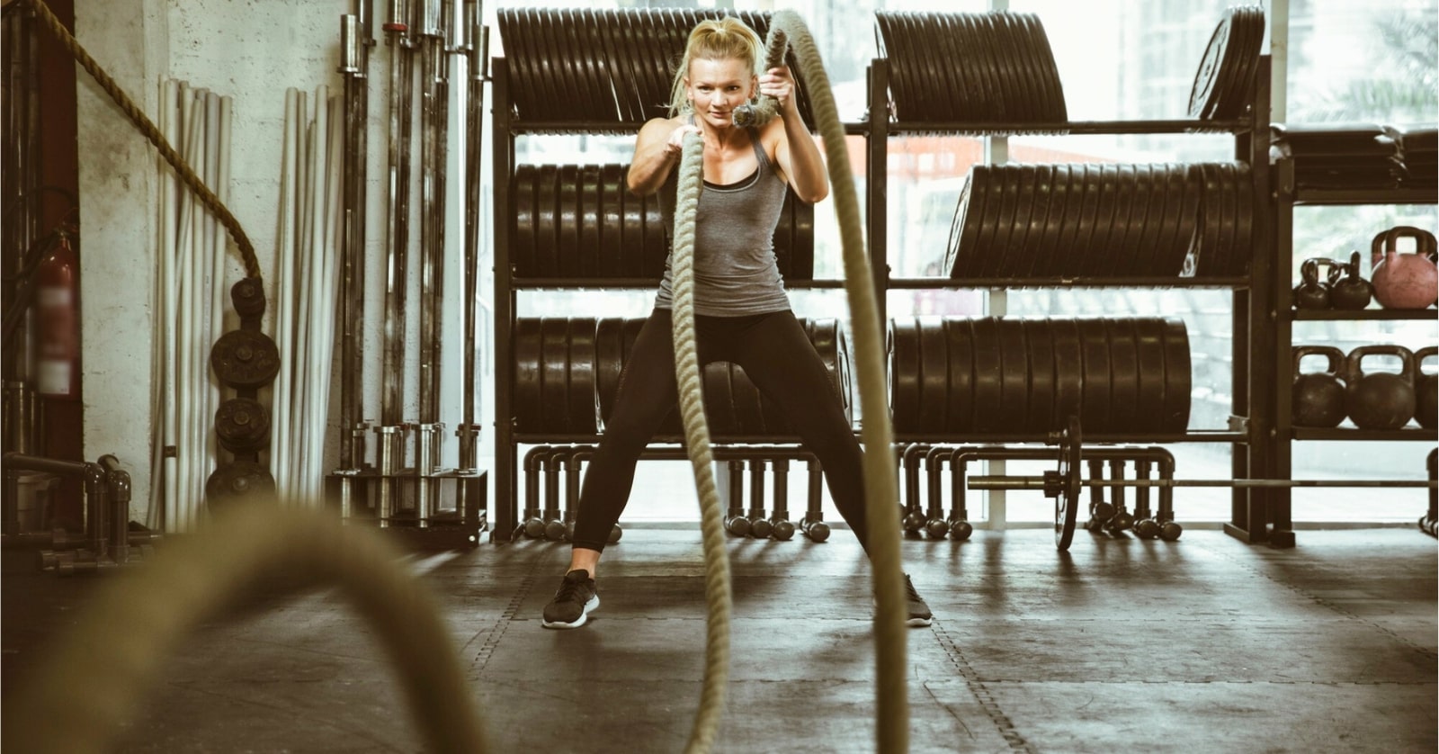 a blonde woman working out in a gym with large ropes