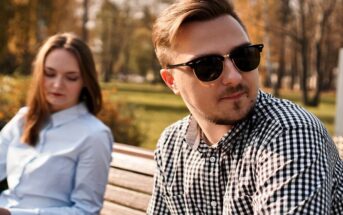 man and woman sitting on a bench outdoors but looking like they have no connection or are distant from one another