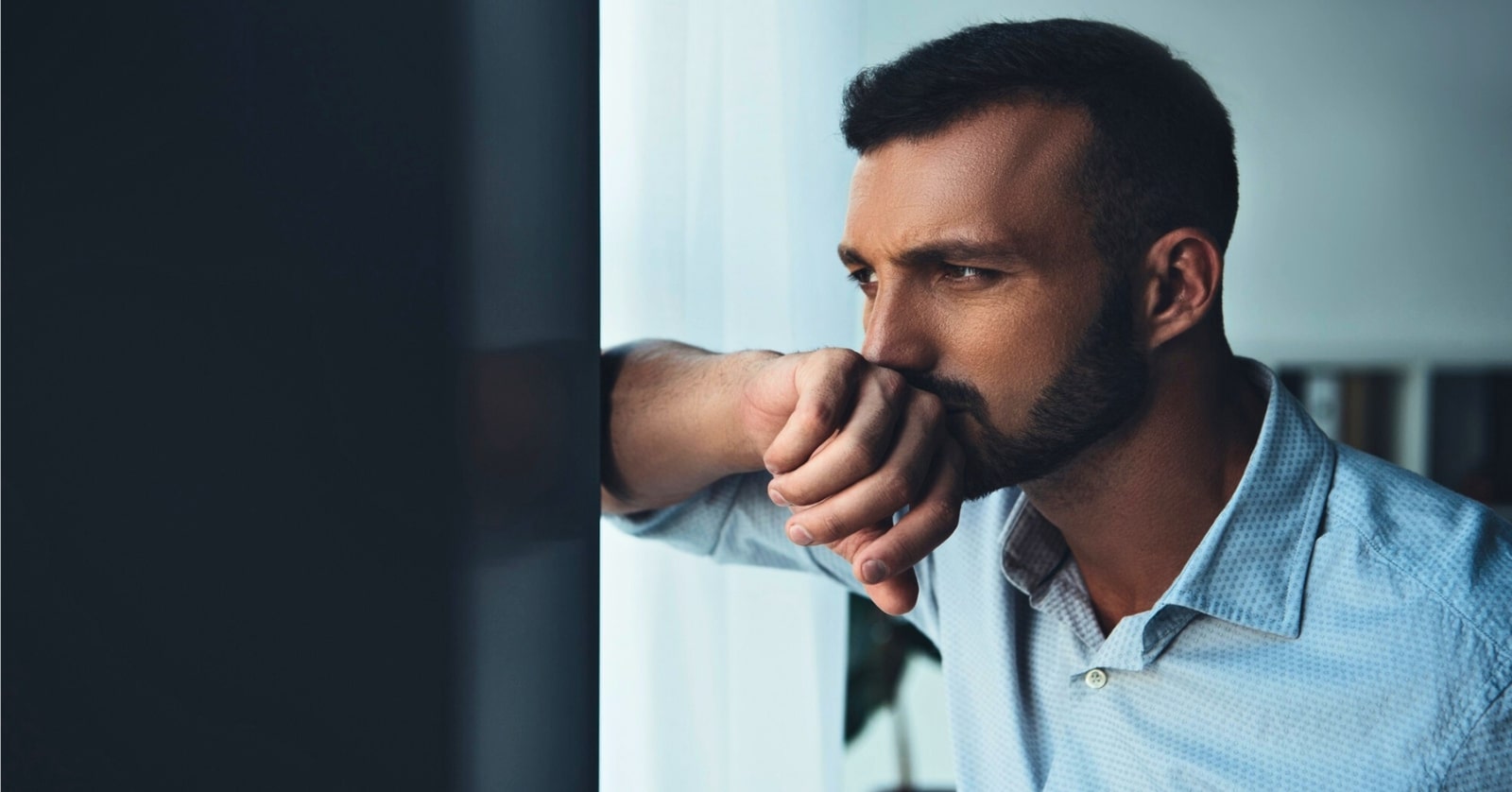 man leaning against wall with the back of his hand over his mouth as if he doesn't want to talk