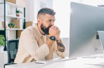 stressed looking man staring at his computer screen in an office environment, illustrating a perfectionist