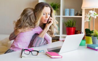 mother with child on her lap sitting at home desk looking at laptop with phone to her ear - illustrating overfunctioning