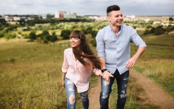 happy couple walking up a grassy hill path with a city in the background