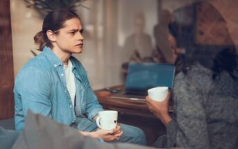 a young woman in a denim shirt looks pensive as her friend opens up about being in the wrong about something