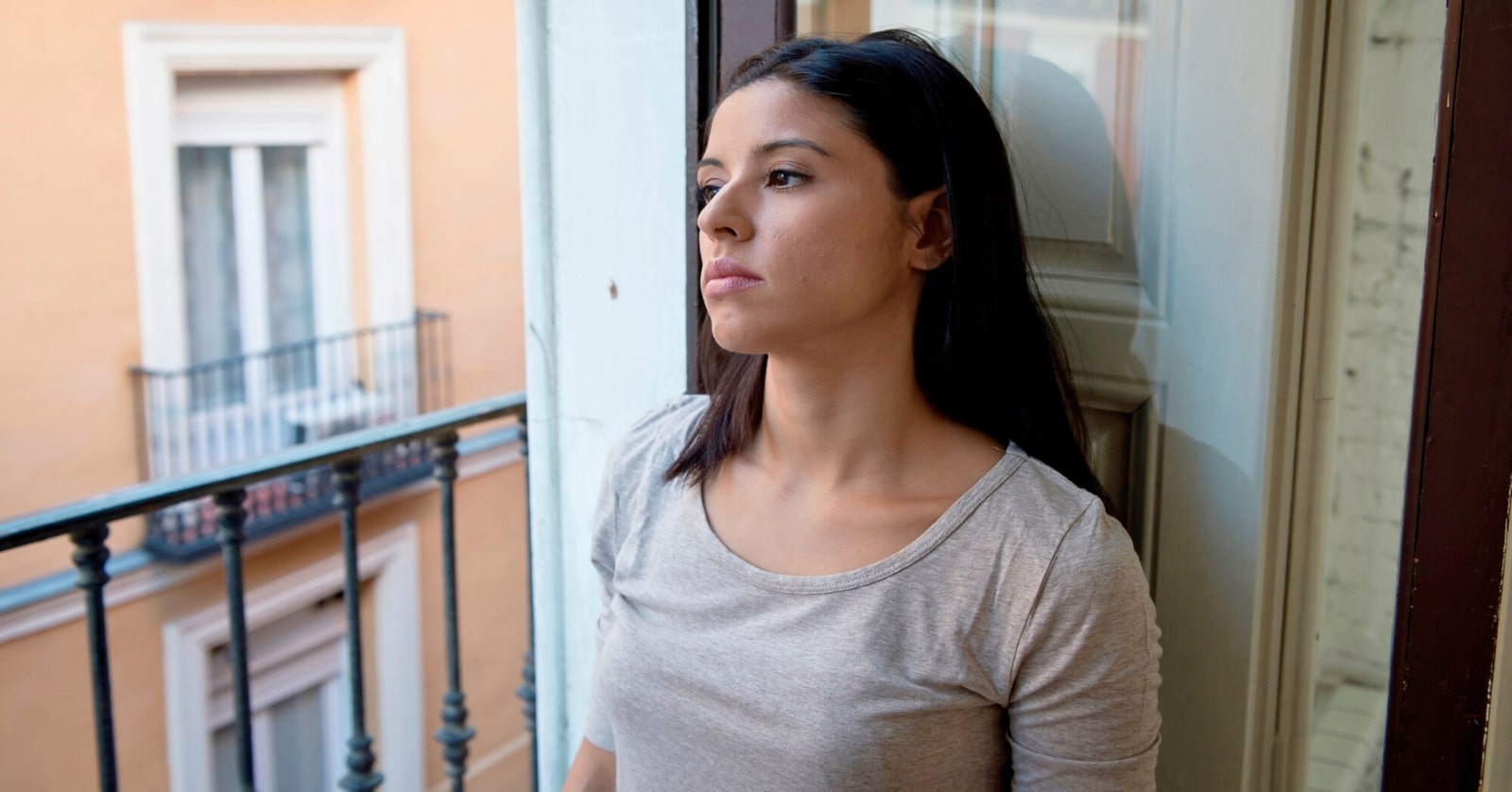 woman sitting by an open window balcony with a sad expression on her face