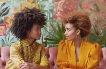 two young women with Afro hair sitting on a couch talking