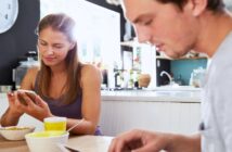 man and woman eating cereal at the kitchen table as they both look at their phones - representing the reality of married life