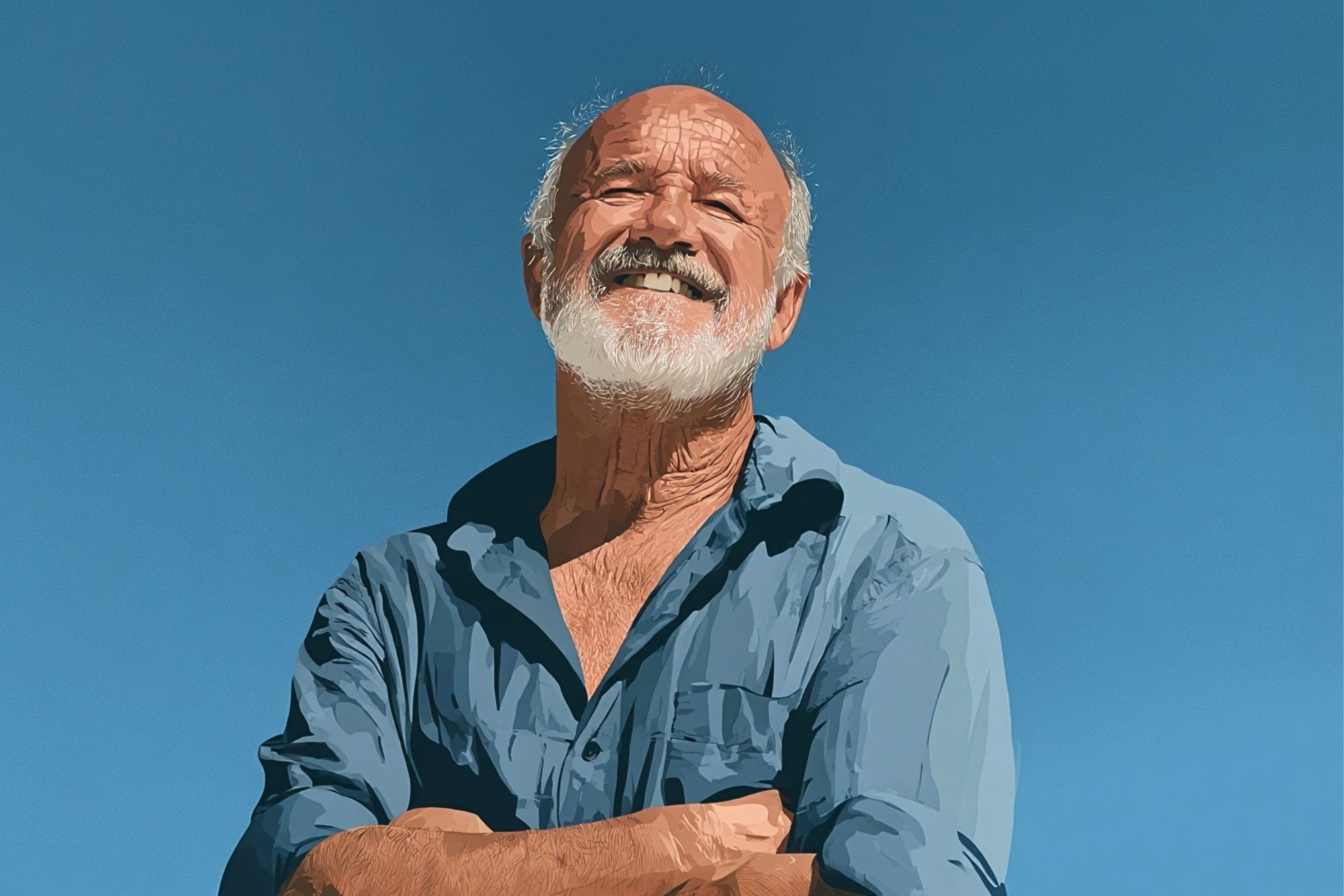 An older man with a white beard and mustache smiles confidently with arms crossed, wearing a blue shirt, standing outdoors against a clear blue sky.