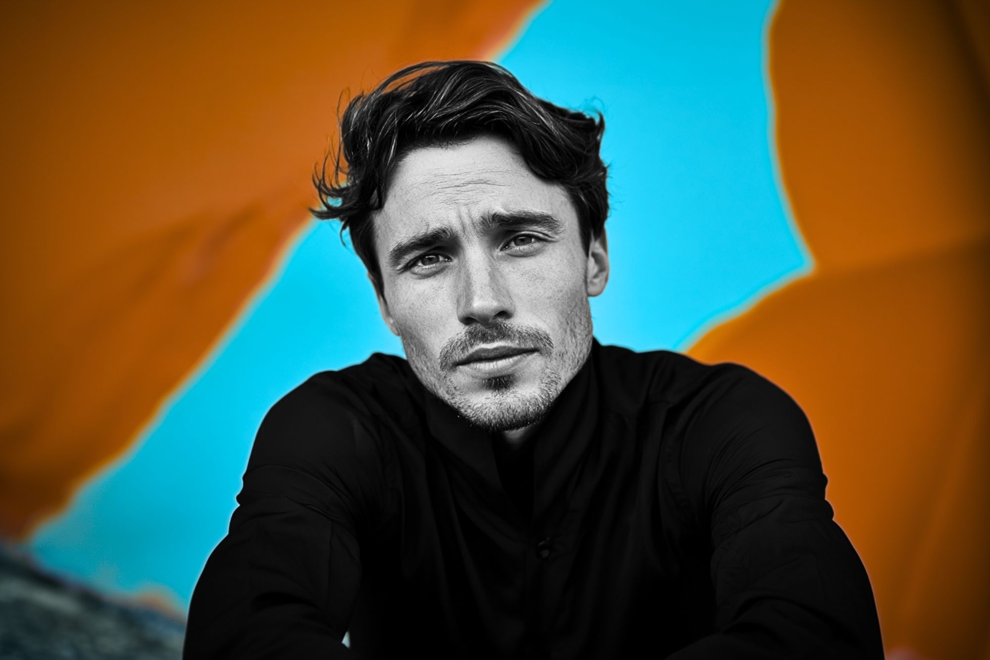 A man in a black shirt looks into the camera with a serious expression; the background is bright blue with large, blurred orange shapes.