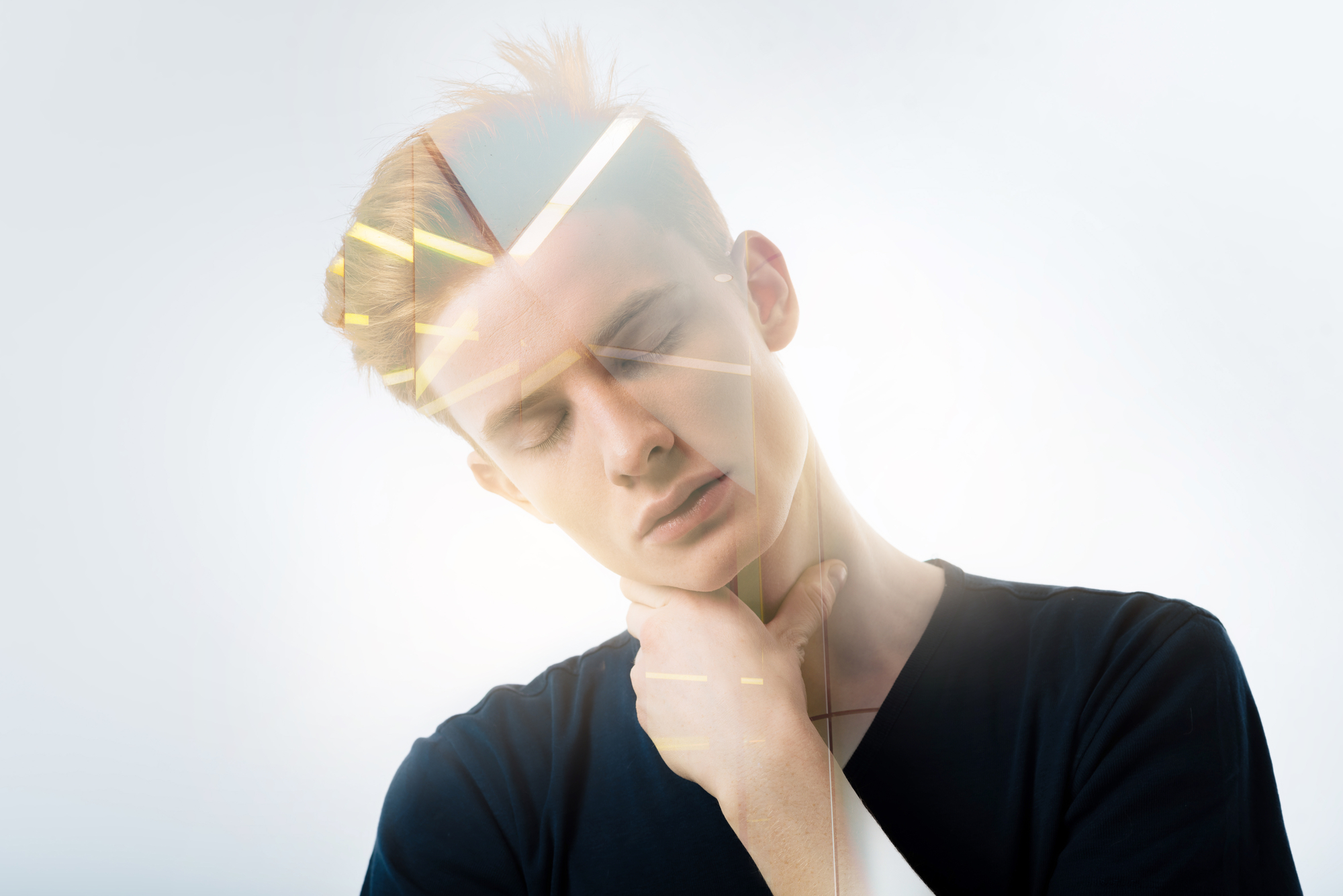 A young person in a black shirt closes their eyes and tilts their head slightly while holding their chin with one hand. The background is a bright white, and there are geometric light reflections overlaying the image, giving it a surreal effect.