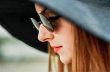 woman looking somewhat forlorn wearing sunglasses and a large black hat
