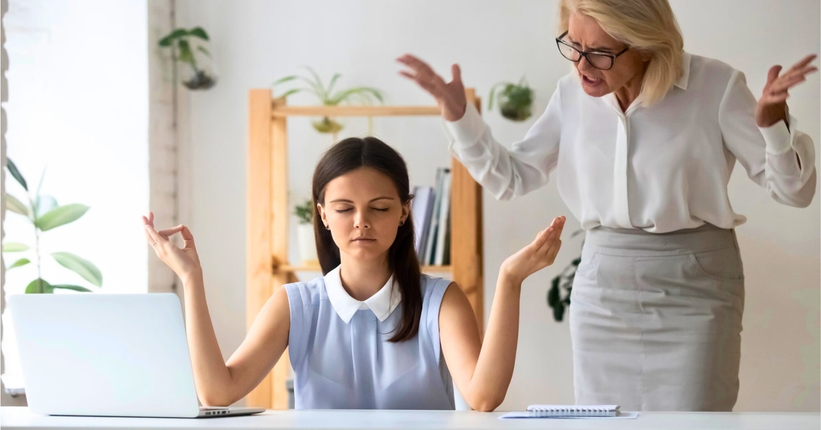 A young woman sits at a desk in a calm, meditative pose with eyes closed, hands raised, and fingers intertwined. An older woman stands behind her, gesturing with frustration. A laptop and notebook are on the desk, and plants decorate the background.