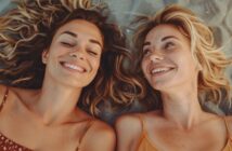 two young women with smiles on their faces as they lay on their backs on the beach