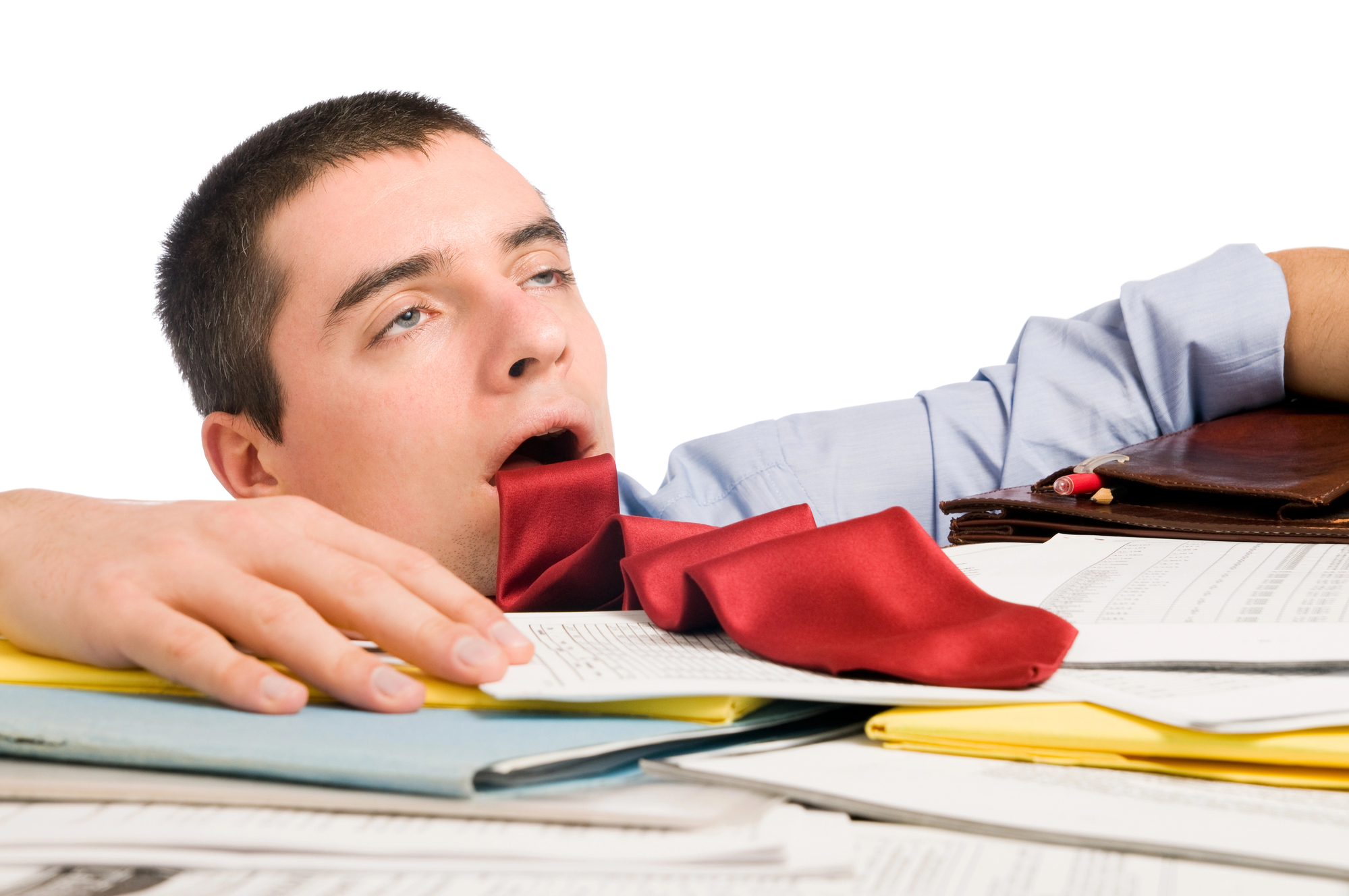 A man with a tired expression leans over a pile of documents on a desk, his eyes half-open and a red necktie seemingly in his mouth. He is resting his head on one hand while the other hand is sprawled out over the papers.