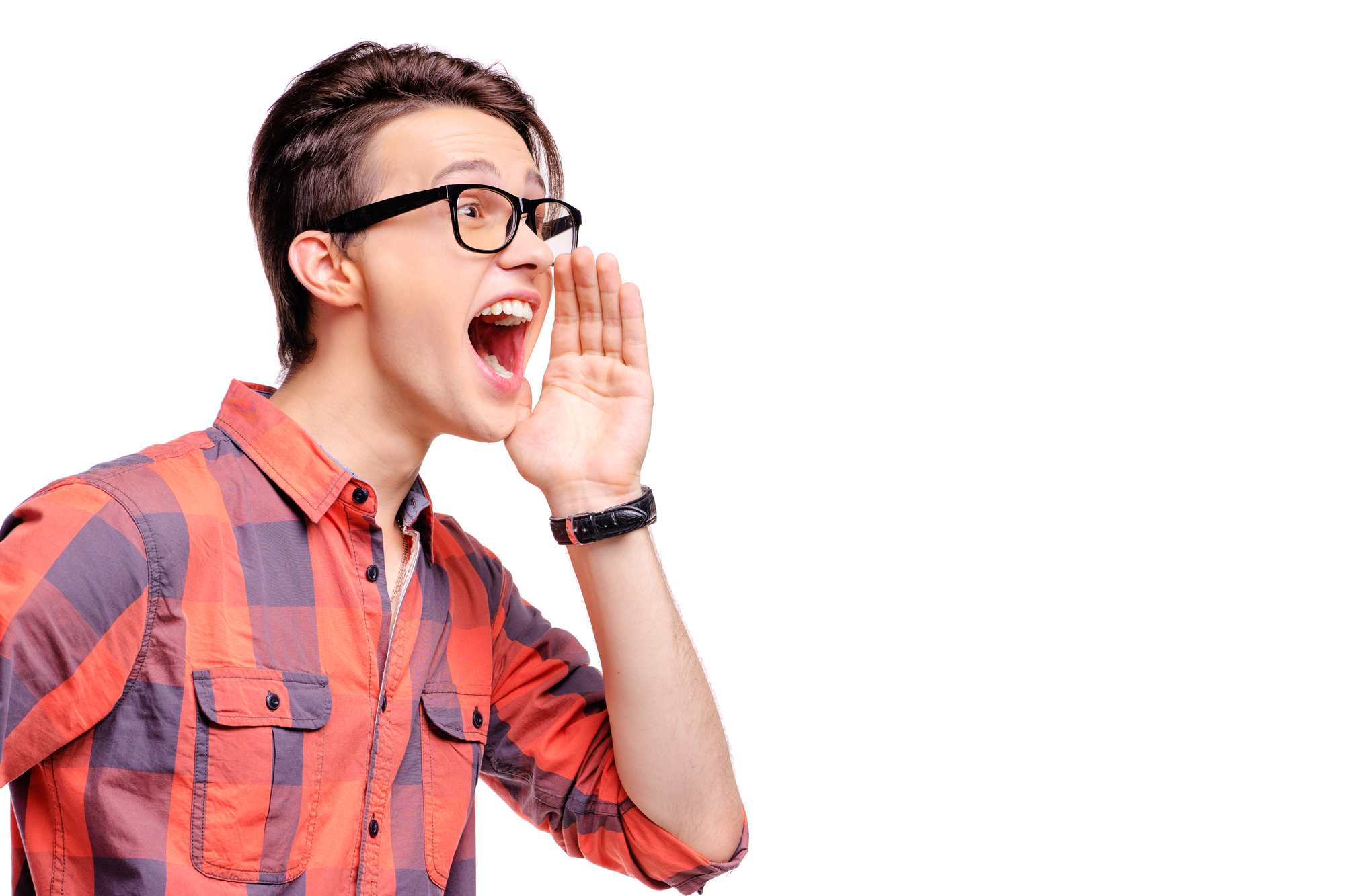 A young man with glasses and brown hair shouts or calls out with his hand cupped to his mouth. He wears a red and blue plaid shirt and stands against a plain white background, appearing enthusiastic or excited.