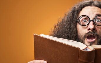 A person with long curly hair and thick-rimmed round glasses is wearing a surprised expression while holding an open book. The background is a solid orange color.