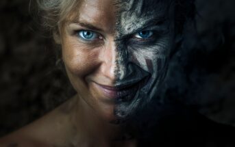 A close-up of a woman with bright blue eyes, half of her face natural and smiling, the other half painted with dark tribal-style markings, creating a dramatic contrast between light and dark sides.