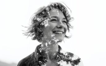A black and white double exposure image of a smiling woman with short hair, blended with the branches and leaves of a tree, creating a harmonious natural effect.