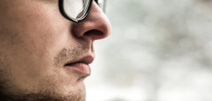 A close-up side profile of a person wearing glasses, with a focused expression. The background is blurred, suggesting an outdoor, possibly snowy setting. The image emphasizes facial details and glasses.