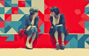 Two women sit on a red bench, facing each other, engaged in conversation. The background features a colorful geometric pattern with red, blue, and cream shapes. Both women wear dresses and have short hair.