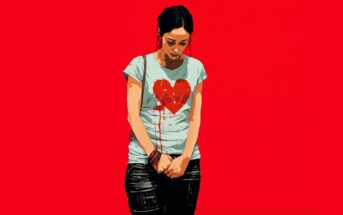 A woman stands against a vivid red background, looking down sadly. She wears a light blue shirt with a bleeding red heart graphic, and dark shorts. Her hands are clasped in front of her, and her expression is somber.