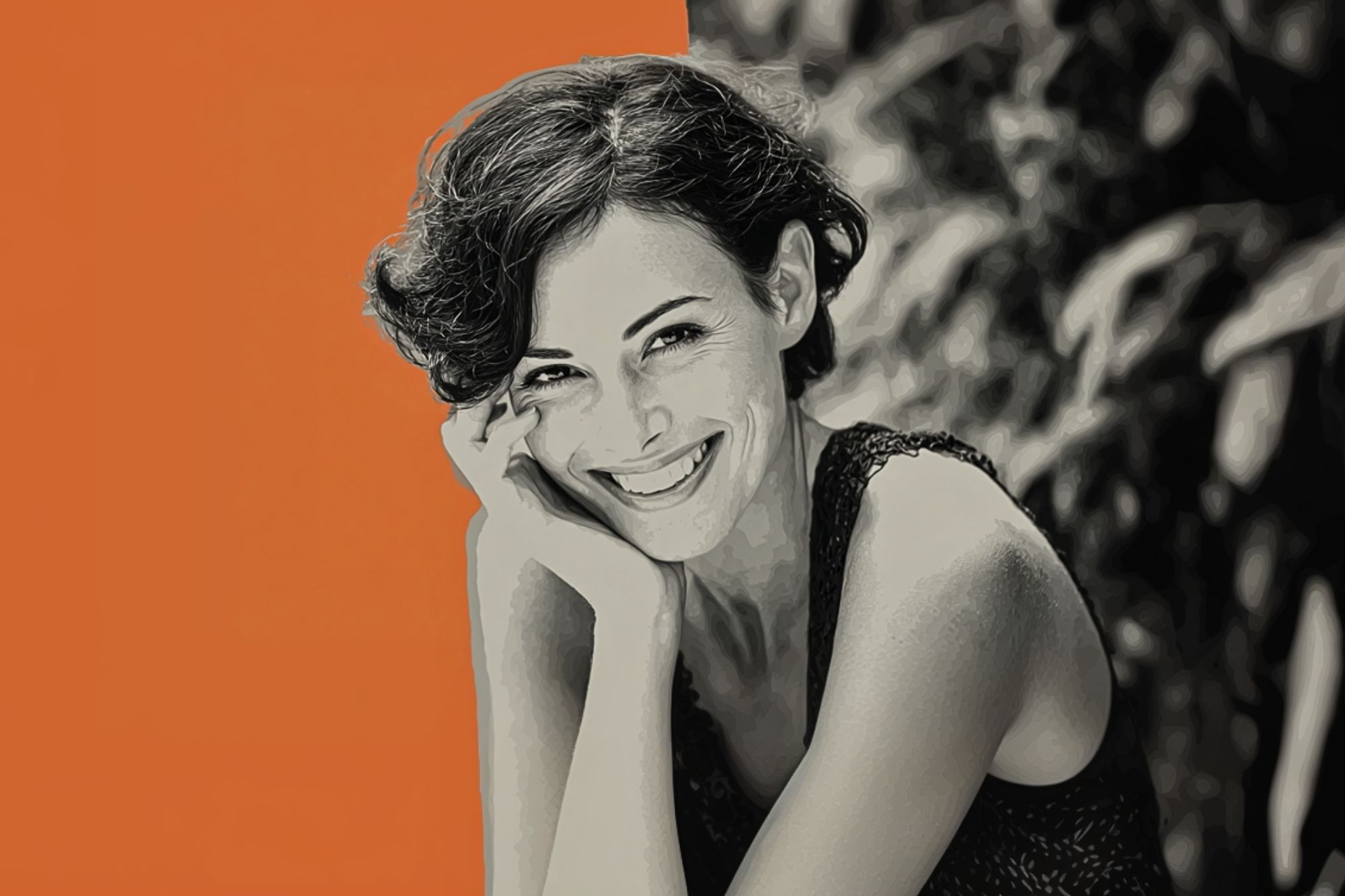 A woman with short, curly hair smiles while resting her head on her hand. The left side of the background is orange, while the right side is black and white with blurred foliage. The image has a painted effect.