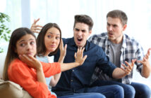 Four people sitting on a couch express intense emotions. The person on the left appears upset, the second person gestures defensively, the third person shouts angrily, and the fourth person argues passionately.