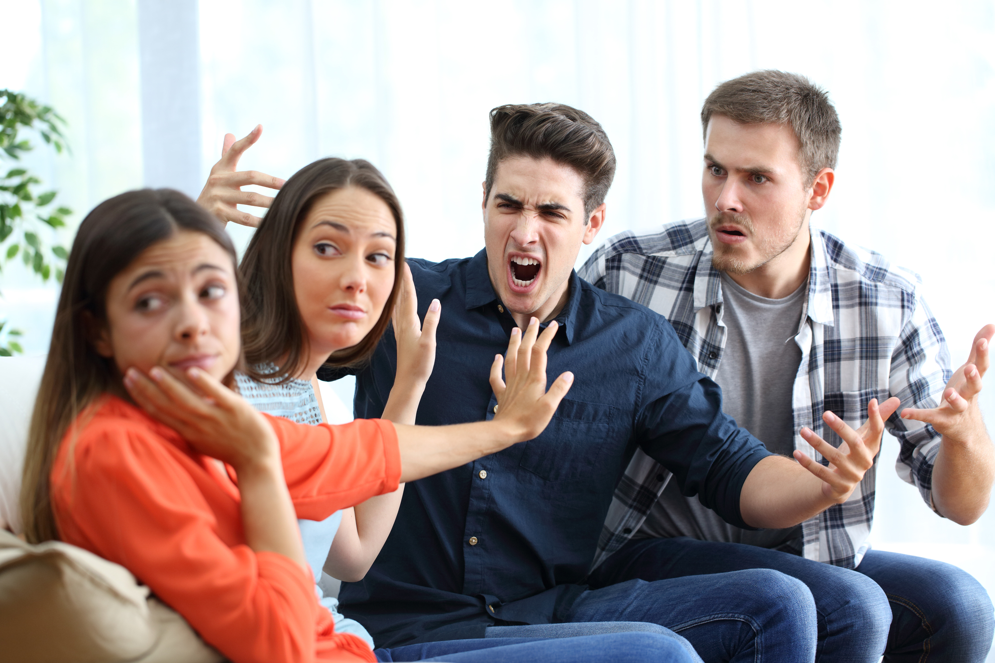 Four people sitting on a couch express intense emotions. The person on the left appears upset, the second person gestures defensively, the third person shouts angrily, and the fourth person argues passionately.