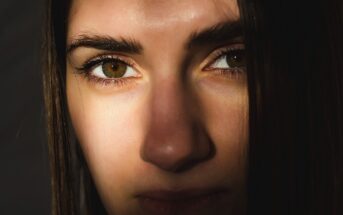8 Disturbing Behaviors That Reveal A Vindictive Narcissist Close-up of a person's face partially in shadow. The focus is on their brown eyes and skin with soft lighting highlighting part of their forehead, nose, and lips. Hair falls on the right side of their face.