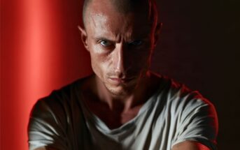 Close-up portrait of a man with a shaved head and intense gaze.