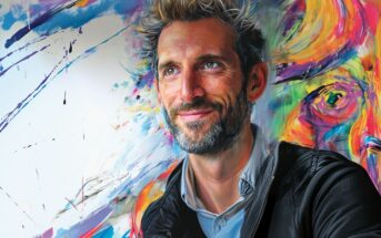 A smiling man with gray hair and a beard, wearing a black jacket, is posed against a colorful, abstract painted background with vibrant brushstrokes and a partial face in the artwork.