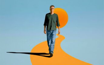 A man in a green shirt and jeans walks toward the viewer on a golden path leading from a large orange sun.
